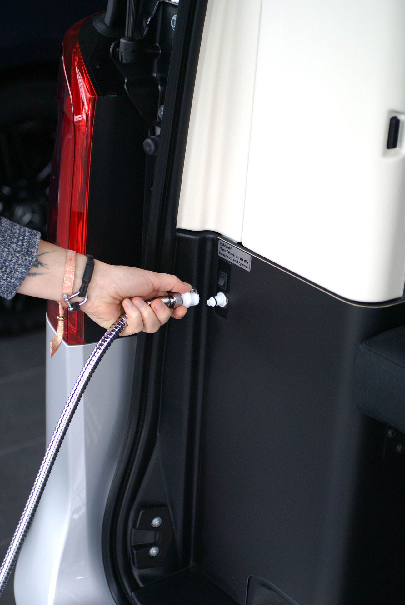 Hebeldusche Camping: Einfacher Anschluss des Duschschlauchs im Camper für unterwegs. Eine Person schließt den silbernen Brauseschlauch der Hebeldusche Camping an den integrierten Anschluss im Fahrzeuginnenraum eines Campers an.