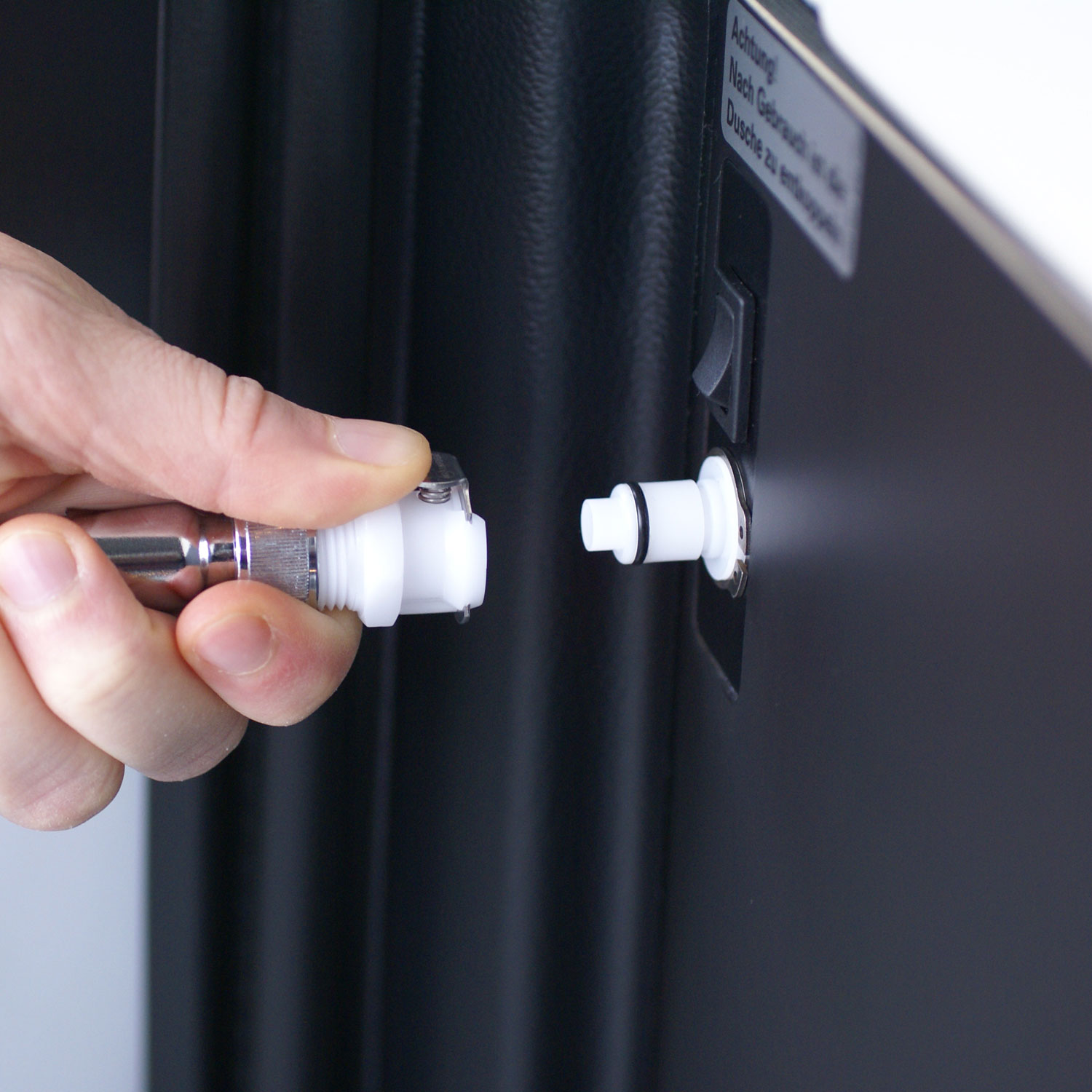 Detailansicht: Einfaches Anschließen des Duschschlauchs an die Hebeldusche Camping für sofortigen Einsatz. Eine Hand verbindet den Duschschlauchanschluss mit dem Hauptgerät der mobilen Hebeldusche Camping. Der weiße Stecker wird in den entsprechenden Port des schwarzen Geräts eingeführt.